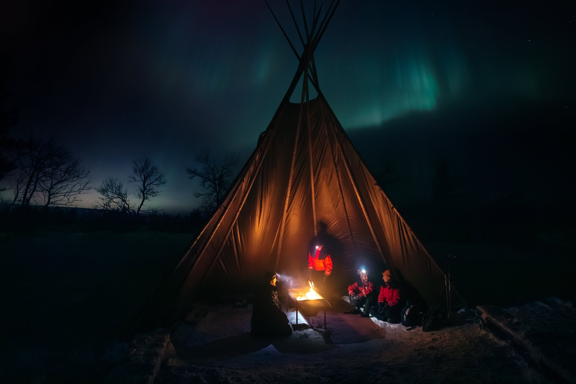 Guests round a fire in a lavvu as the northern lights glow overhead